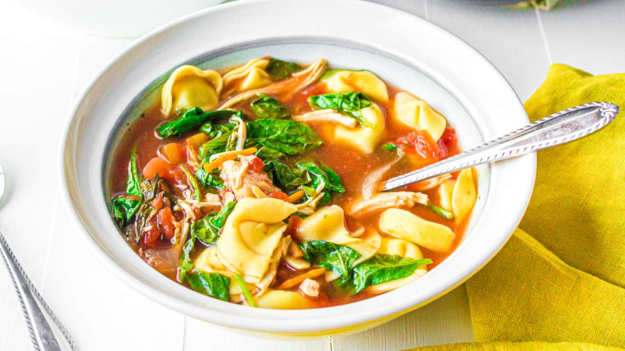 Bowl of tomato chicken and tortellini soup with a spoon in the bowl