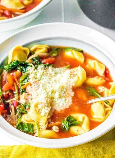 A bowl of tomato soup with tortellini, spinach and cheese