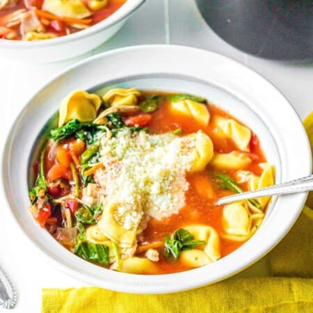 A bowl of tomato soup with tortellini, spinach and cheese
