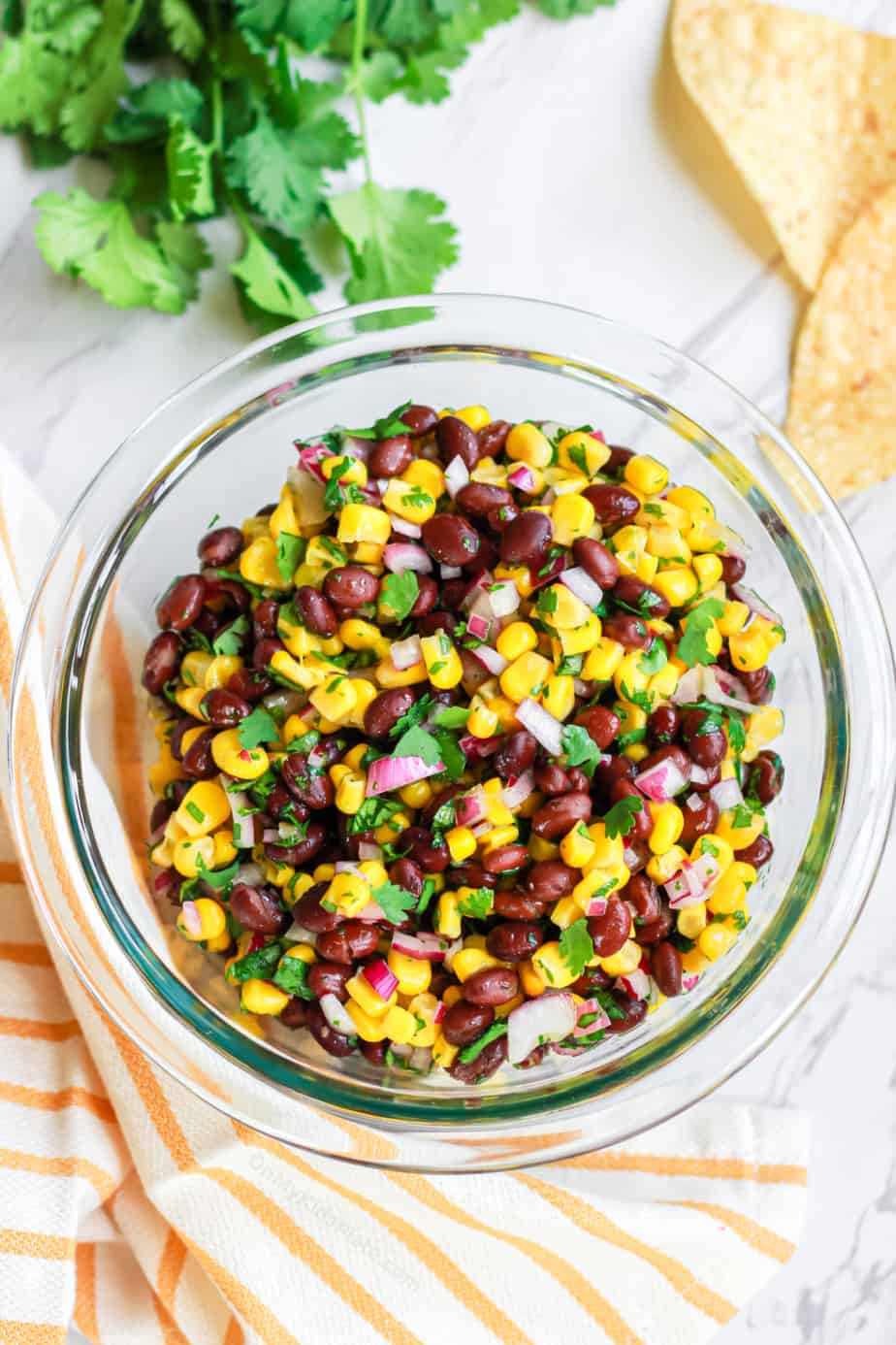 Black bean corn salsa in a bowl with chips and cilantro on the counter