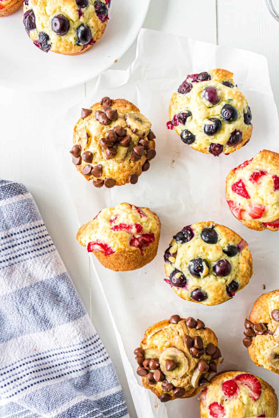 Strawberry, chocolate chip banana and blueberry muffins on parchment paper to serve.