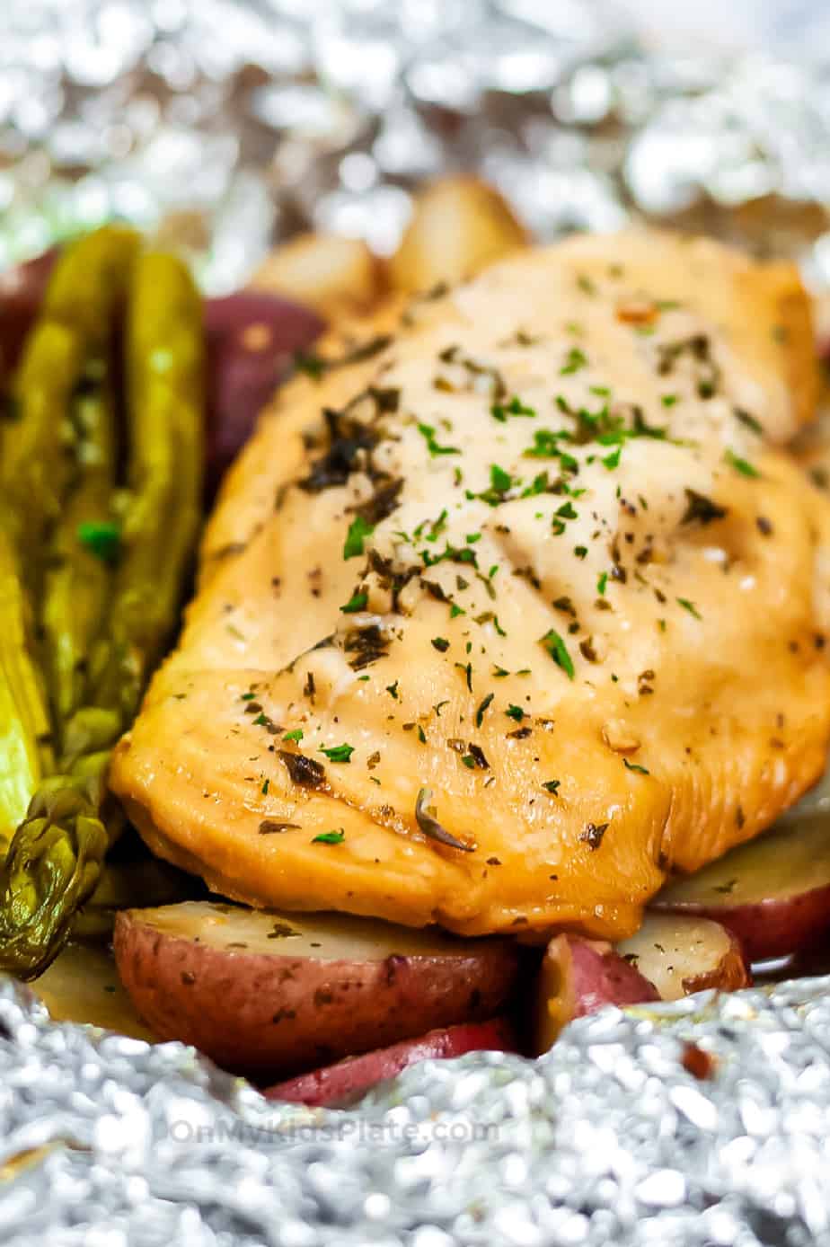 Close up of cooked chicken, asparagus and potatoes in a foil packet from the side.