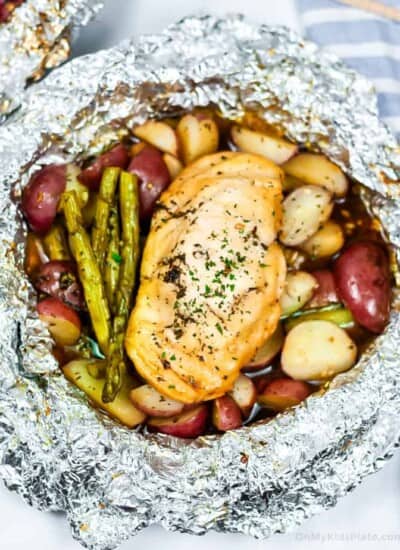 An open foil packet from the grill with chicken, potatoes and asparagus cooked inside