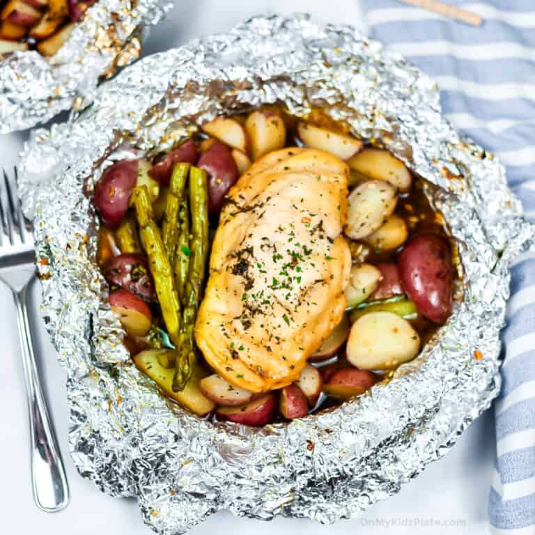 An open foil packet from the grill with chicken, potatoes and asparagus cooked inside