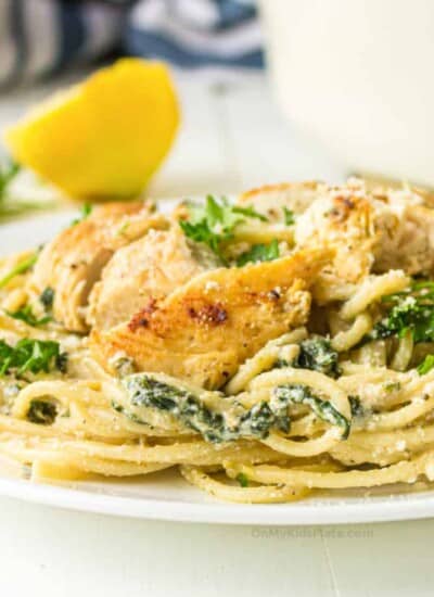 Chicken and spinach with spaghetti in a cheese sauce with lemon in the background