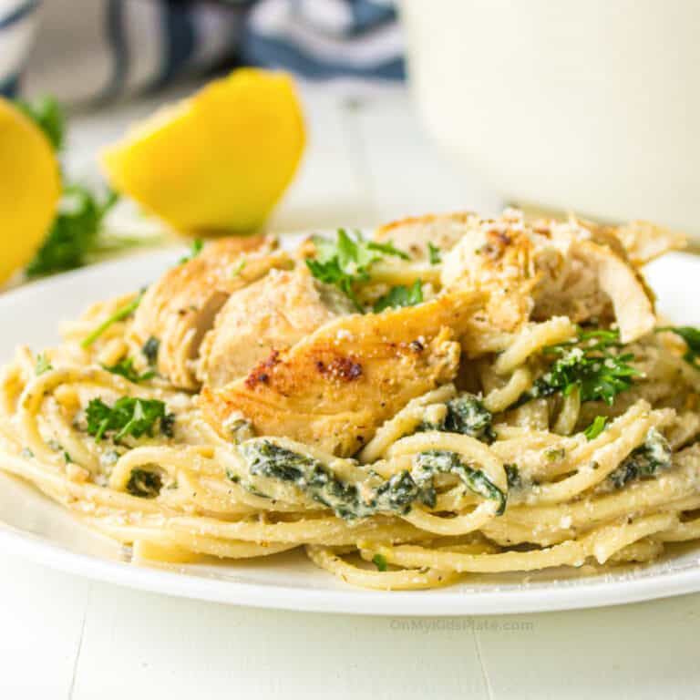 Chicken and spinach with spaghetti in a cheese sauce with lemon in the background