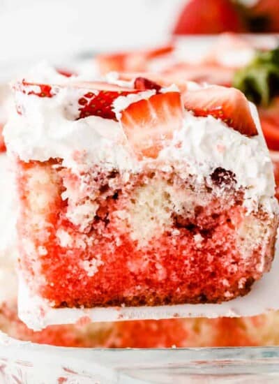 Slice of red swirled cake with strawberries being lifted from the pan.