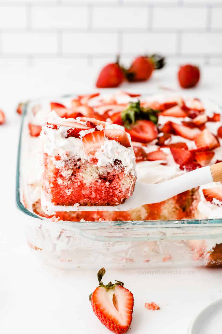 A slice of red and white swirled cake topped with strawberries being lifted out of a glass pan.