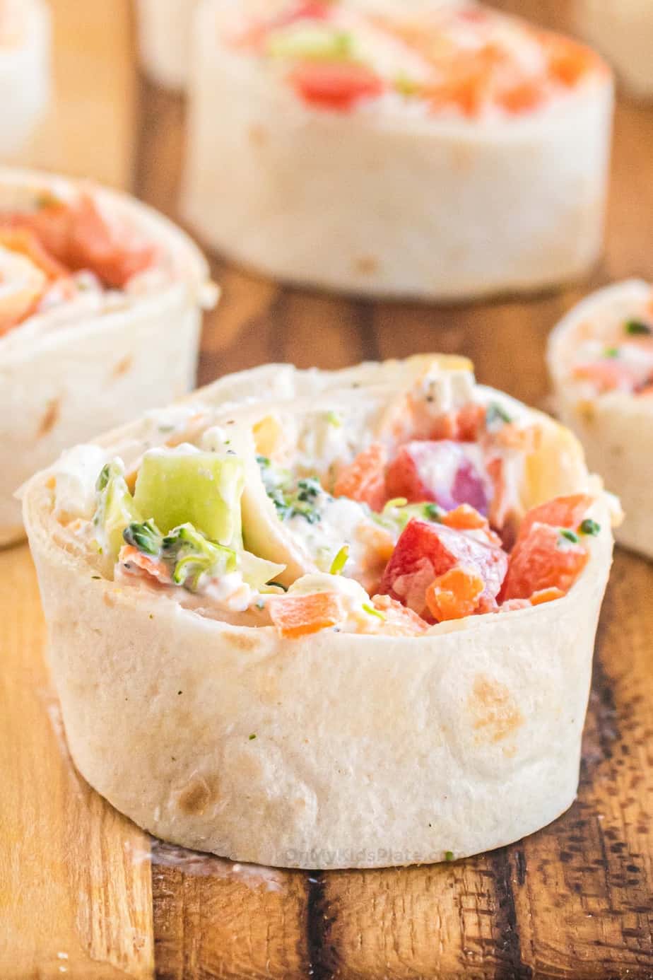 Close up of a tortilla wrapped in a pinwheel around cream cheese and vegetables.
