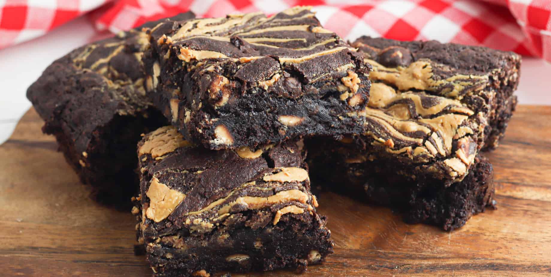 Fudgy chocolate brownies with a peanut butter swirl stacked on a cutting board