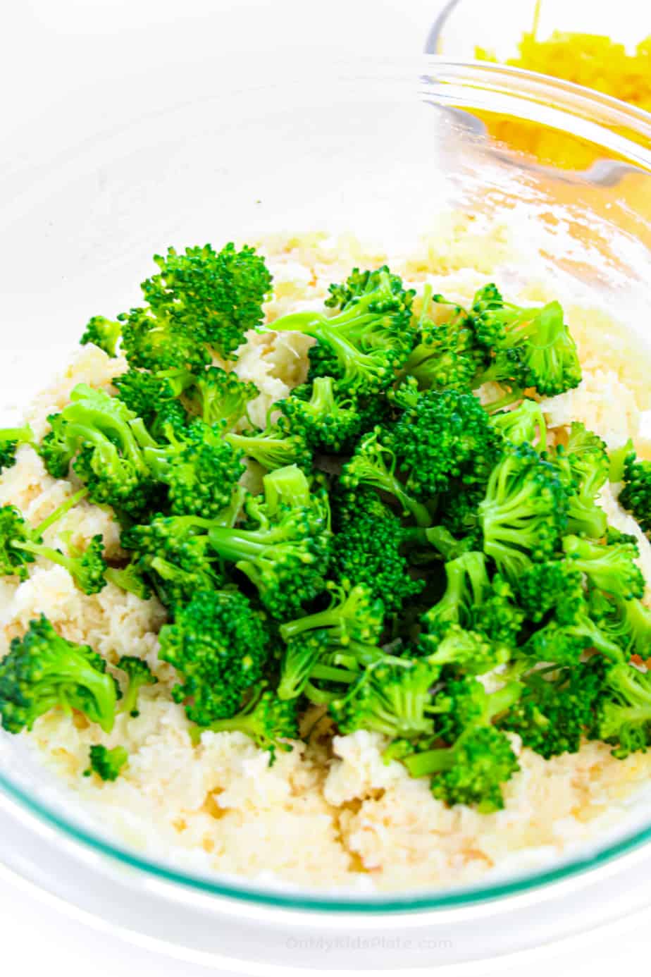 Broccoli being added to a mashed potato mixture in a bowl.