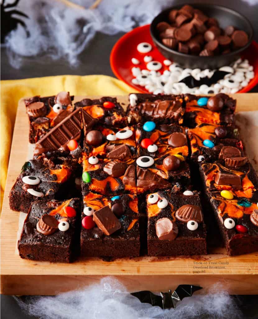 Brownies covered in Halloween candy and an orange swirl sliced on a cutting board.