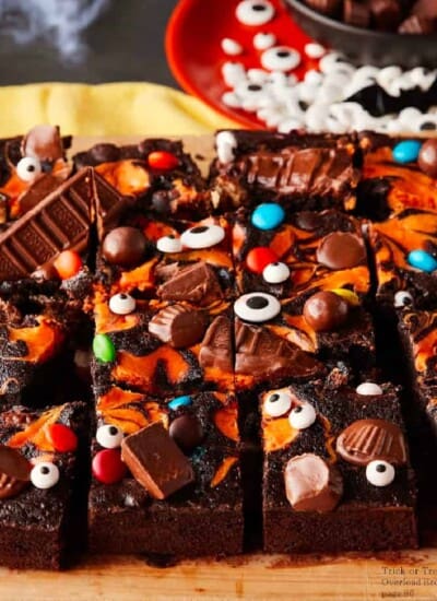 Side view of brownies covered in an orange cream swirl, chocolate candy and candy eyes for Halloween on a cutting board