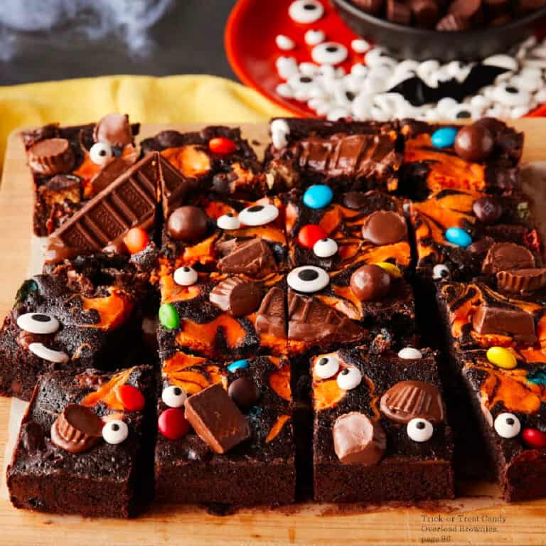 Side view of brownies covered in an orange cream swirl, chocolate candy and candy eyes for Halloween on a cutting board