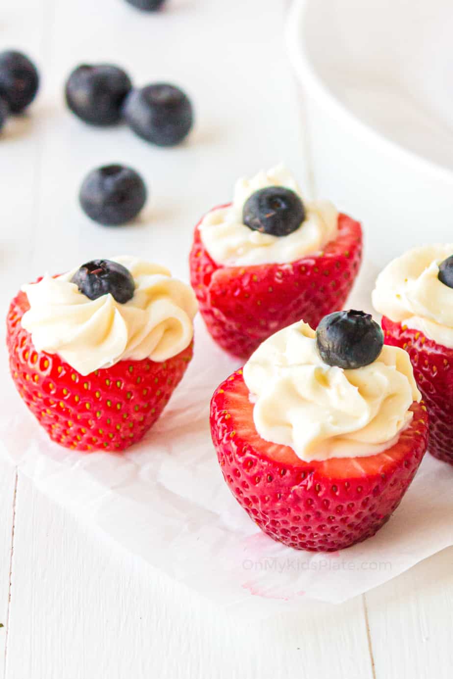Side view of three strawberries filled with cheesecake and topped with a blueberry