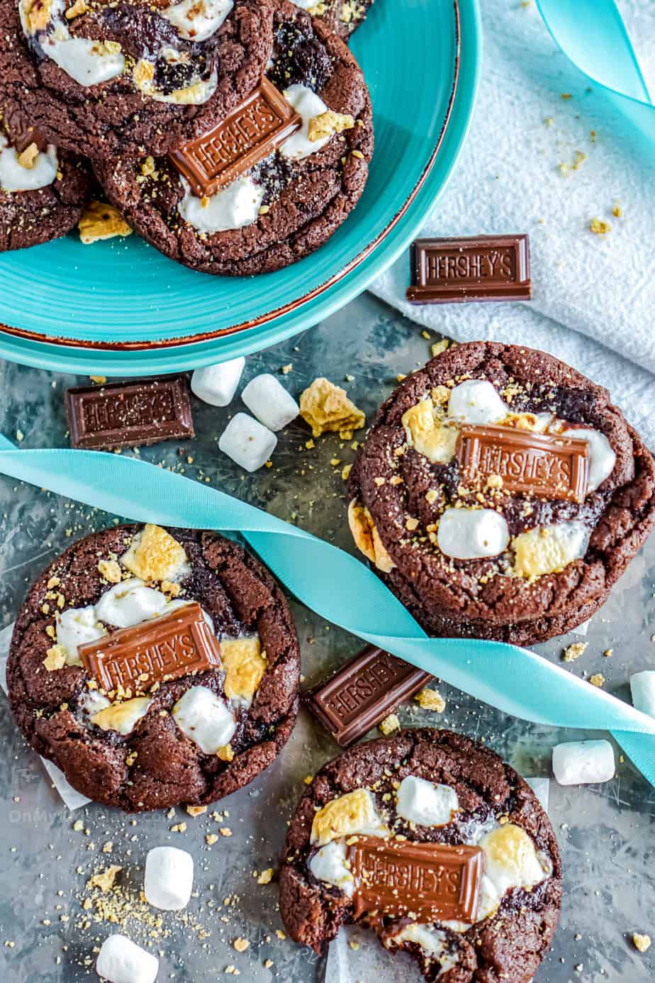 chocolate marshamllow smores cookies on a plate and on a table, one cookie with a bite.