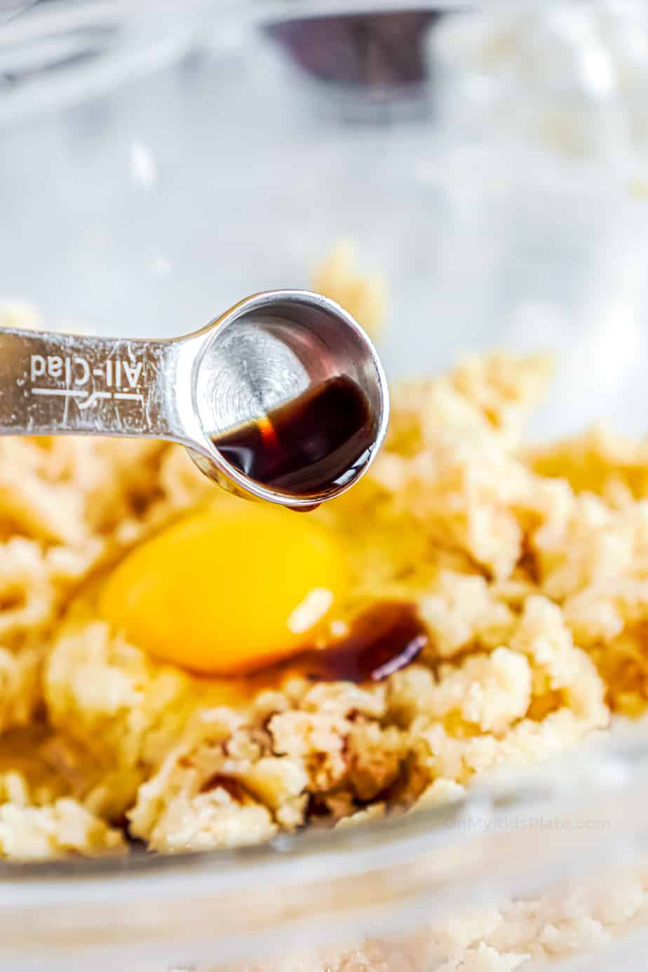 Pouring vanilla on top of a cracked egg and cookie dough mixture in a bowl.