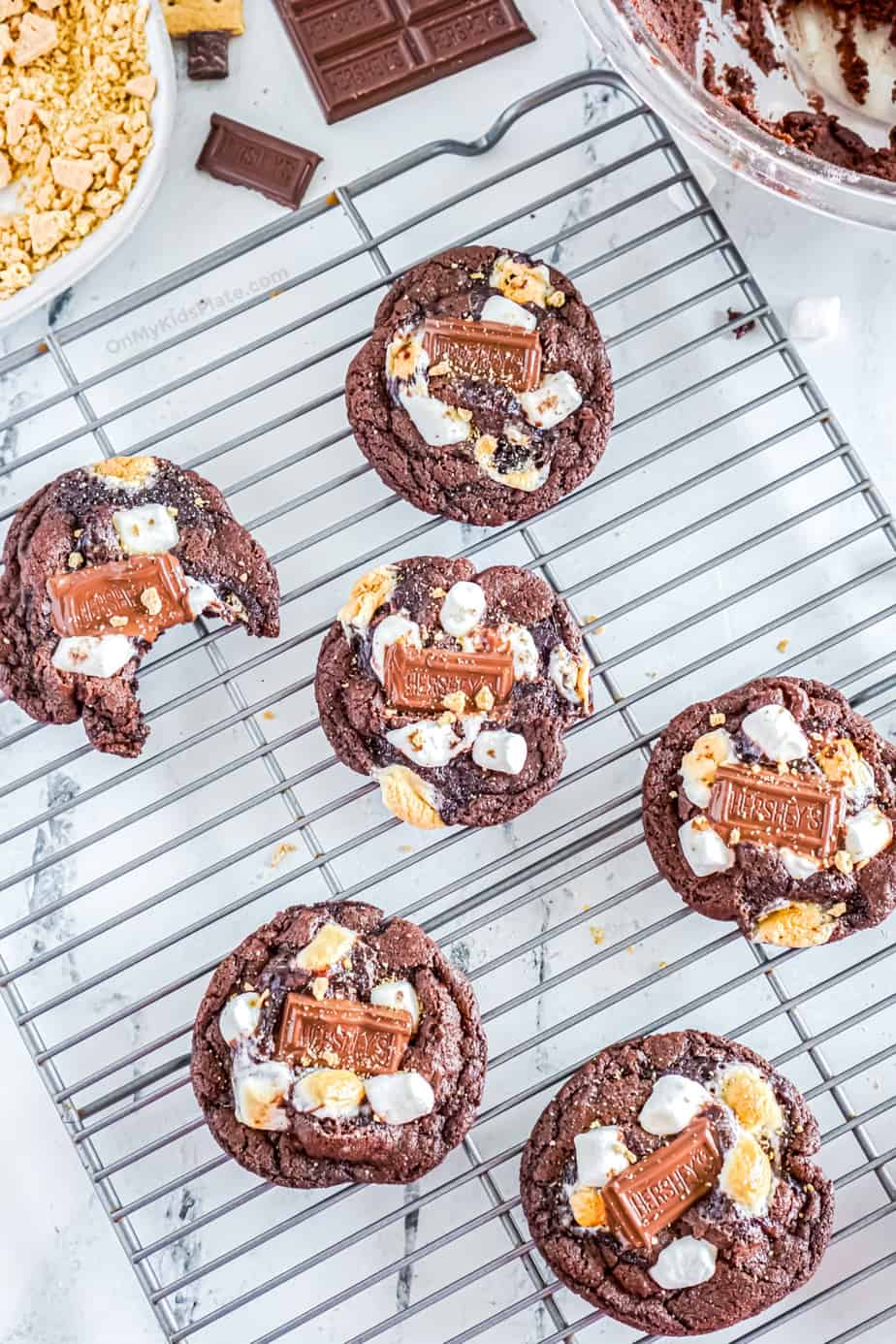 Chocolate S'mores cookies cooling on a rack, one has a bite missing.
