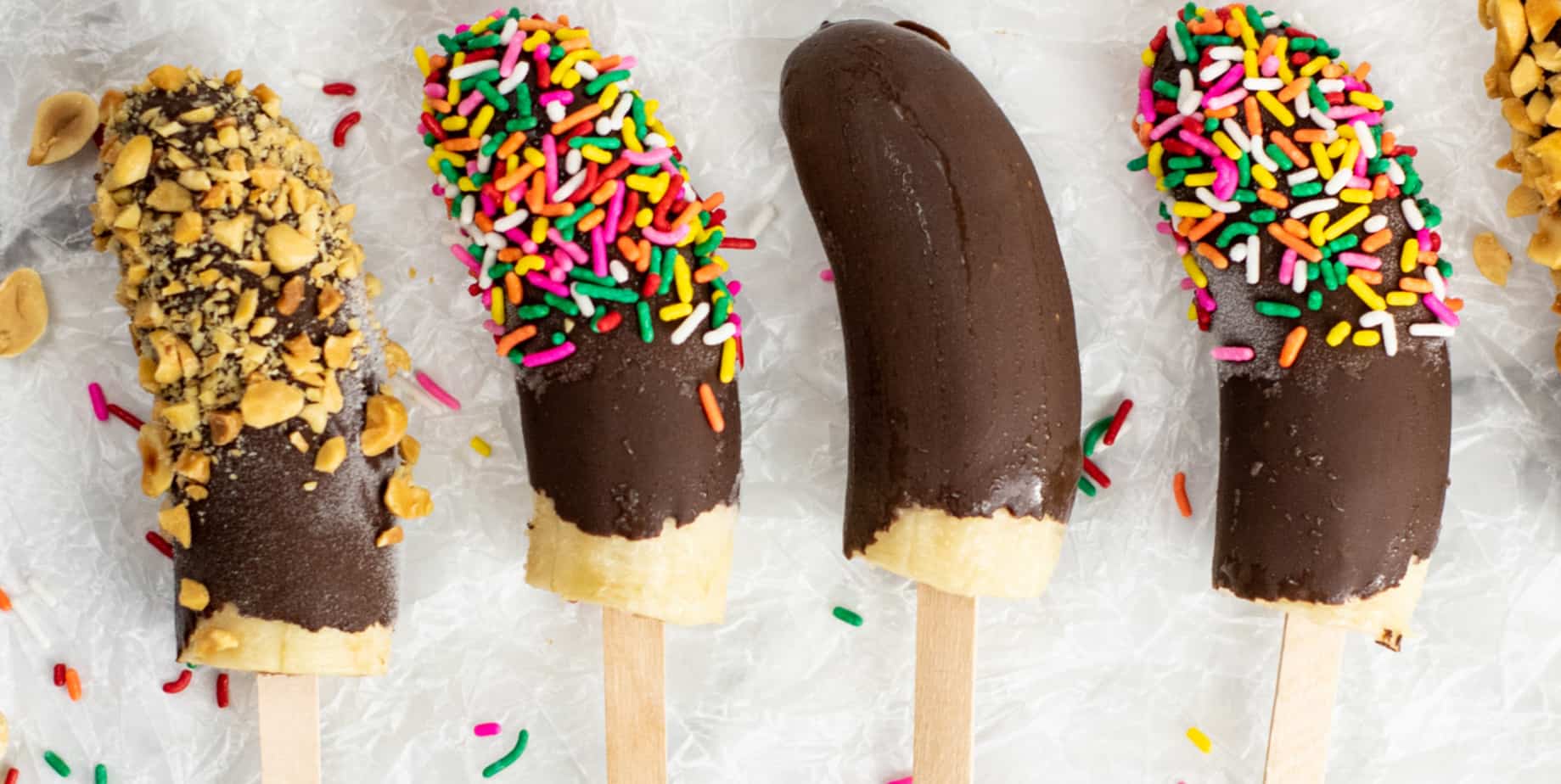 Four chocolate dipped bananas decorated with peanuts and sprinkles