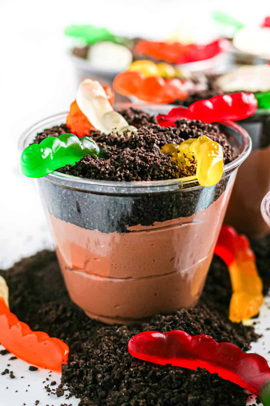Chocolate pudding layered with oreo crumbs and gummy worms in a clear cup from the side