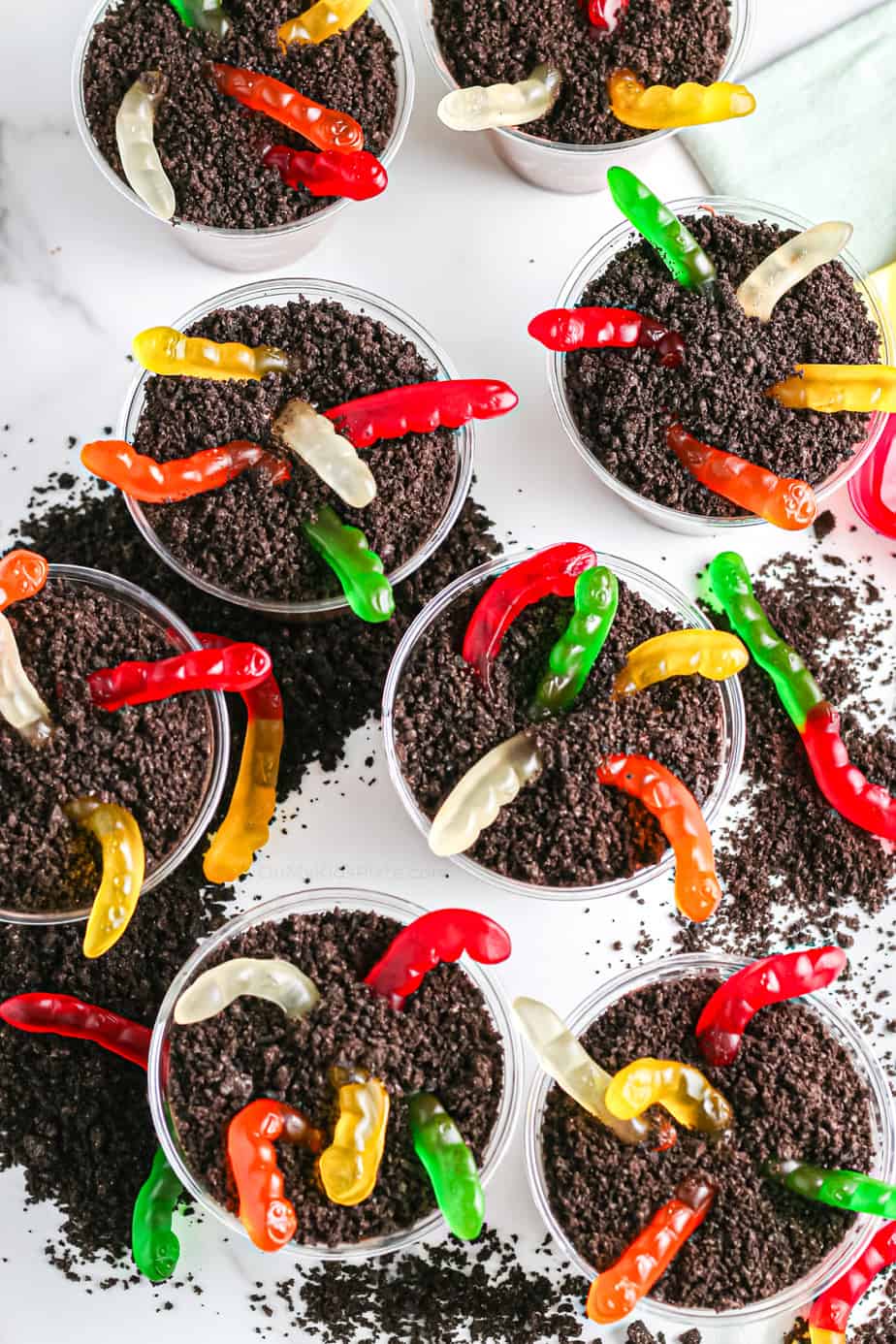 Chocolate dirt pie individual cups with gummy worms from overhead with chocolate cookie crumbs scattered around the cups.