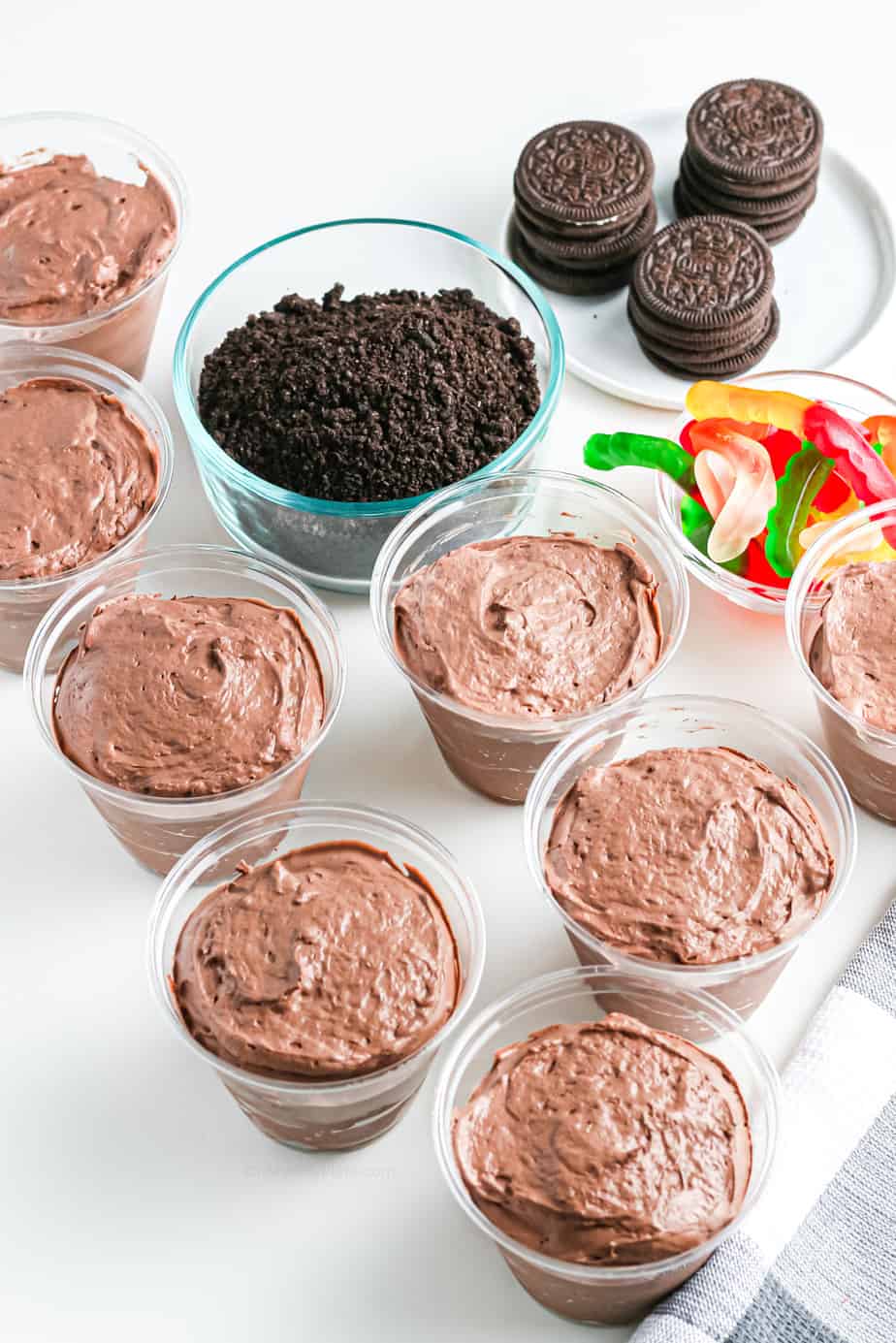 Chocolate pudding in individual cups with Oreo chocolate cookies and gummy worms in bowls