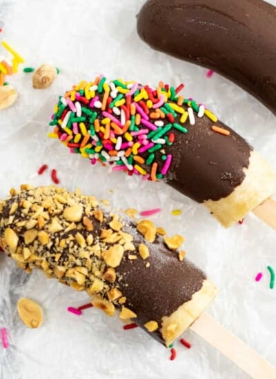 Three frozen bananas on popsicle sticks with nuts, sprinkles and chocolate