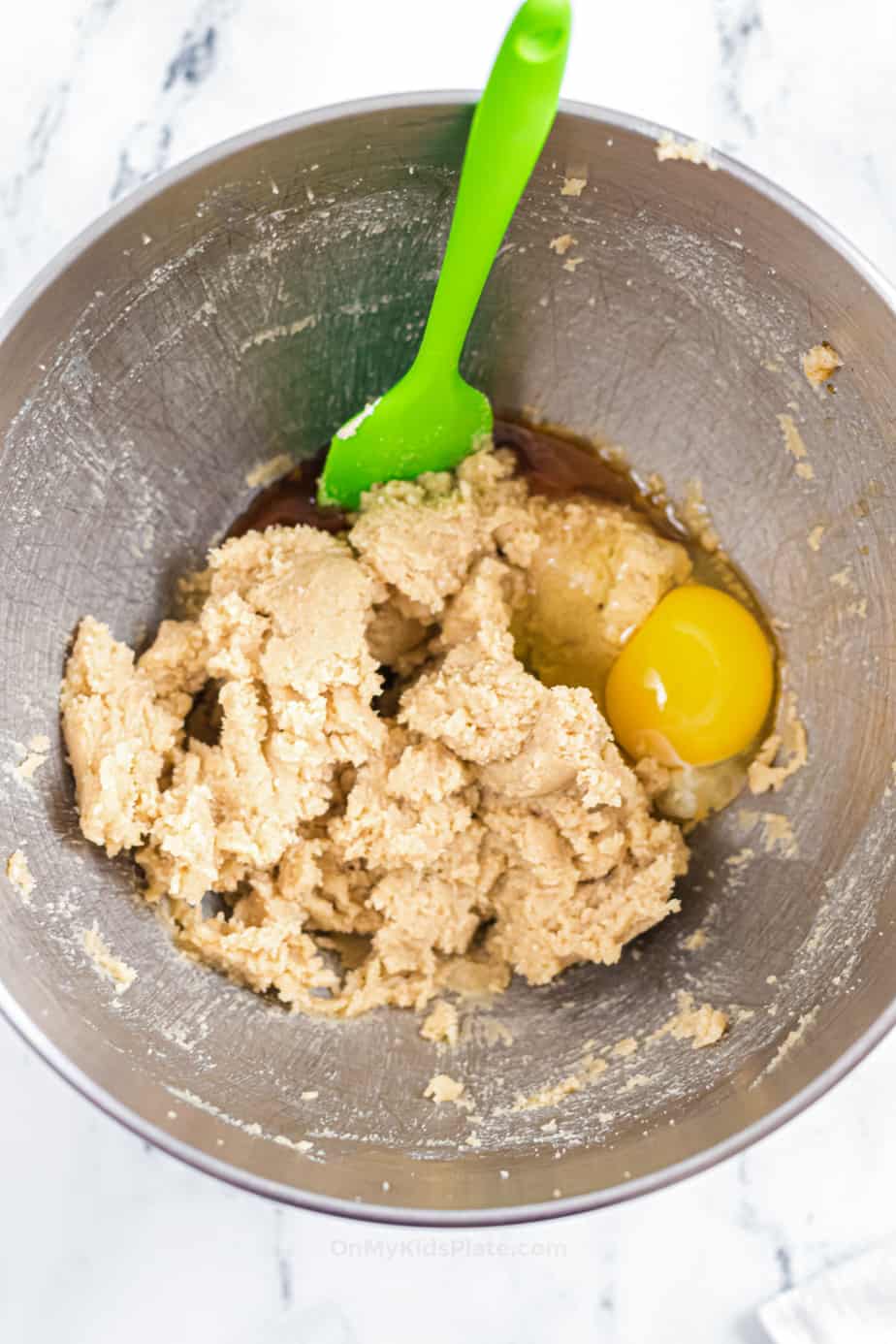 Eggs and vanilla being mixed into cookie dough batter in a bowl.