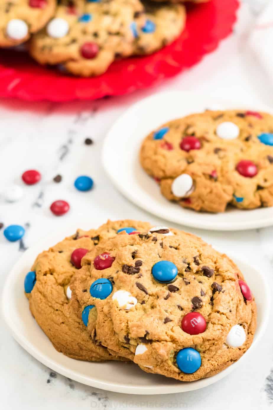 Cookies with red white and blue M&Ms on two plates with a platter of cookies behind