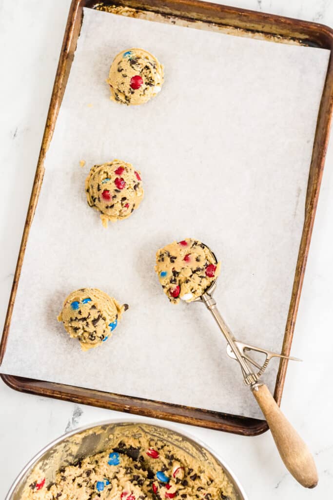 Cookie dough being scooped from a bowl to a baking sheet.