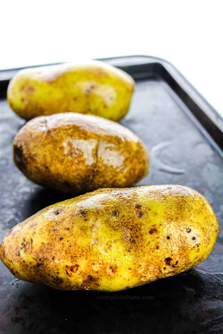 Three potatoes on a baking sheet rubbed with oil