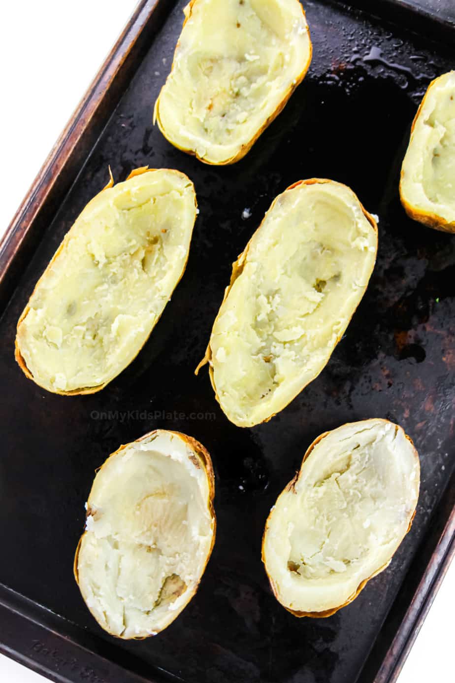 Cooked potato halves on a pan that have had the soft potato inside scooped out.