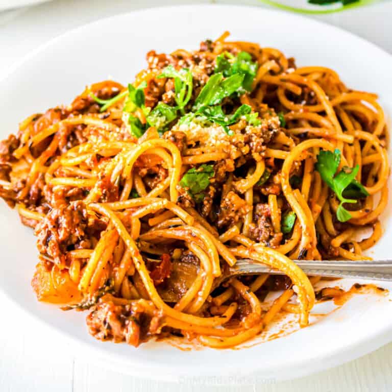 Close up square image of pasta in a tomato ground turkey sauce on a plate with cheese and parsley.