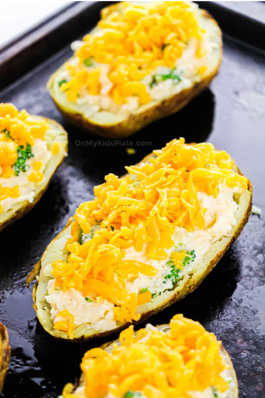Twice baked potatoes stuffed and topped with shredded cheese on a baking pan.