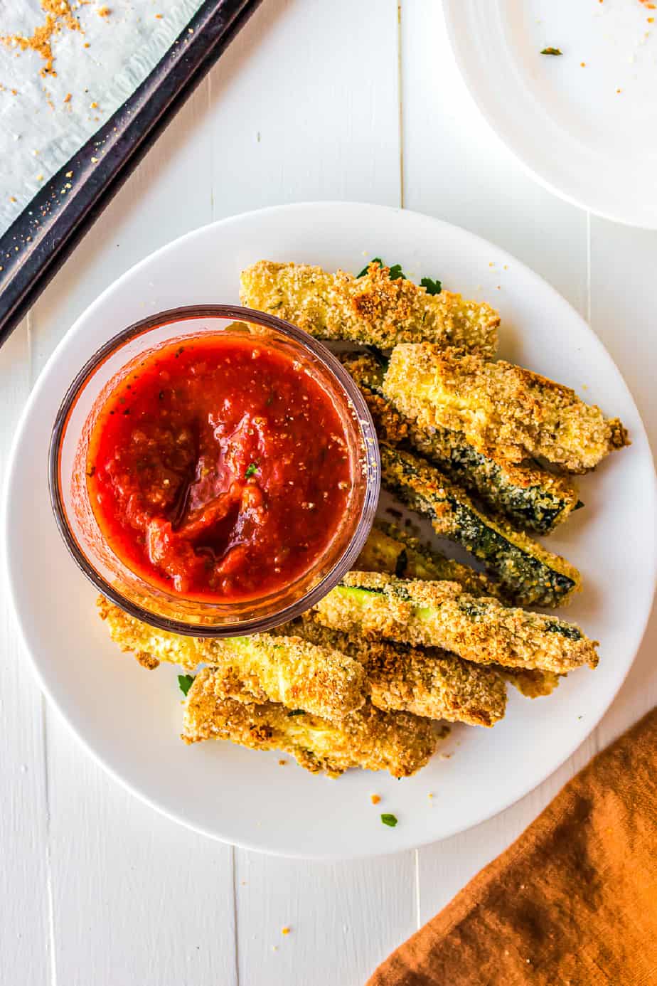 Zucchini fries from overhead on a plate with a bowl of marinara sauce.