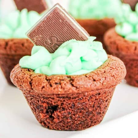 Close up of a chocolat4e cookie cup filled with frosting and a chocolate mint candy on a serving tray