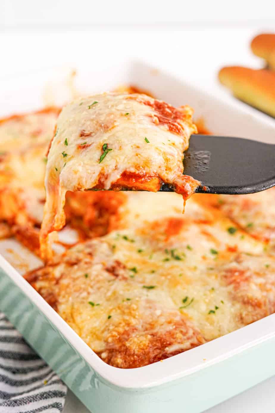 A serving of baked ravioli covered in cheese being pulled out of a casserole dish with a spatula