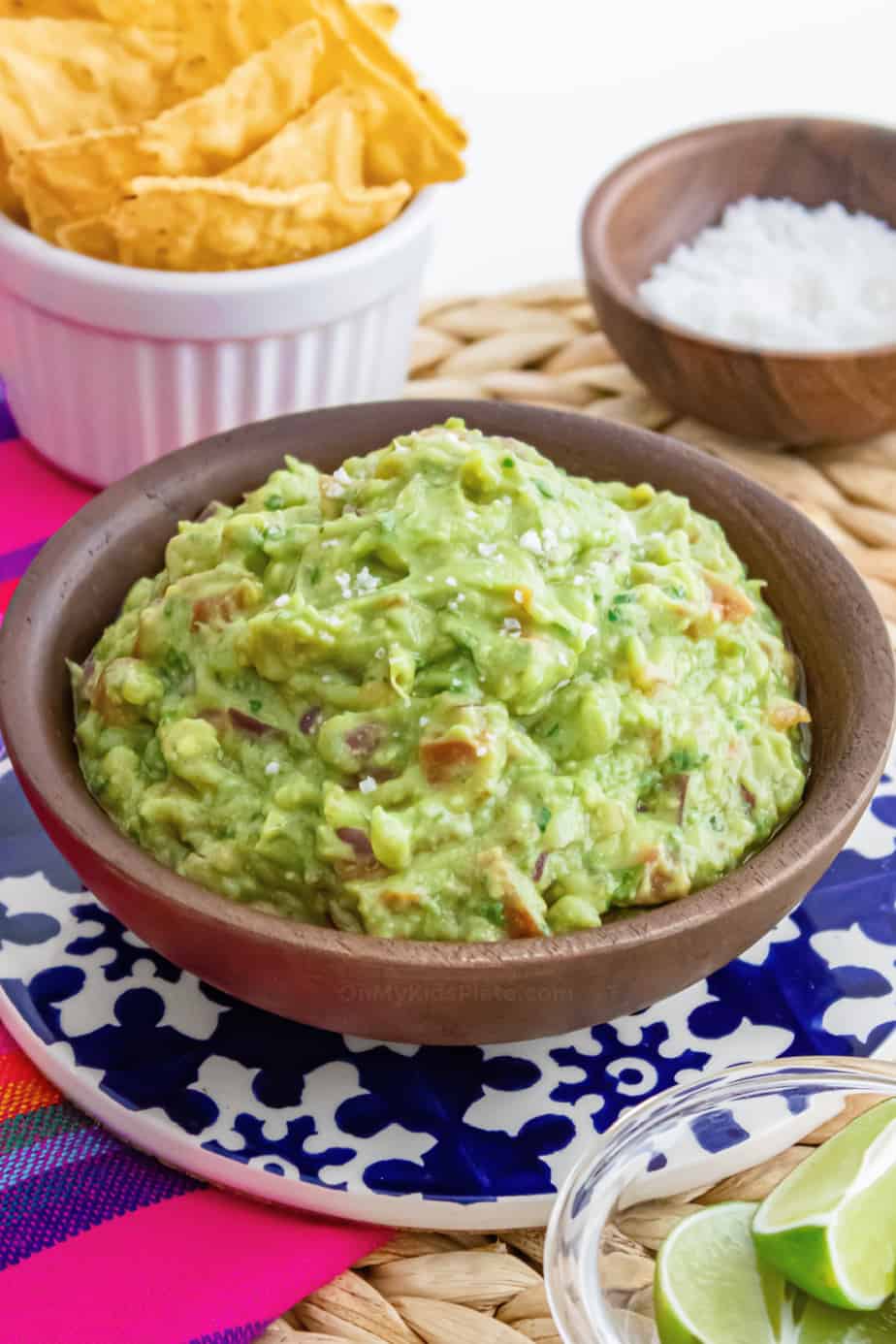 Guacamole in a wood bowl with small bowls of chips, salt and lime.