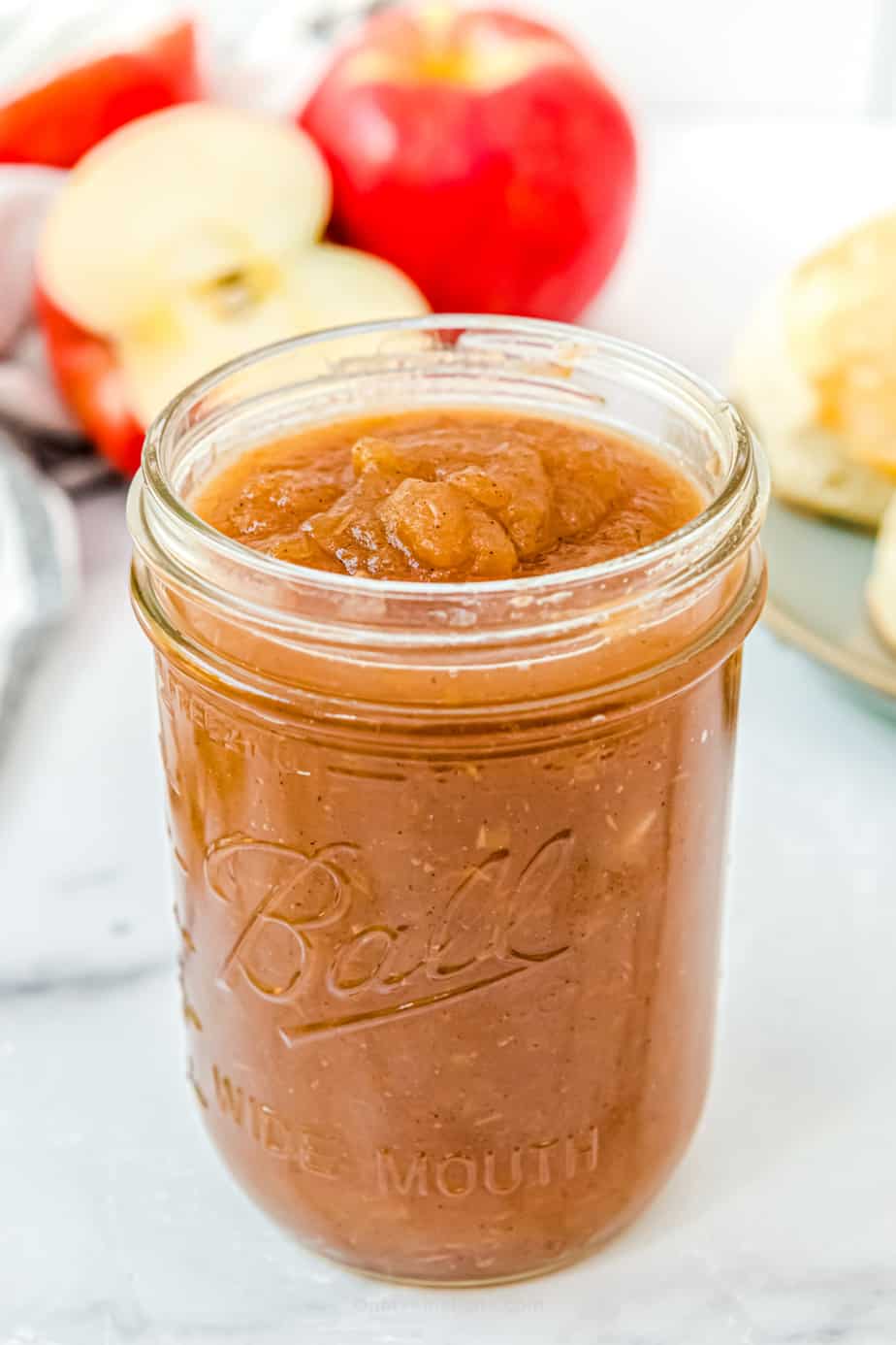 Apple butter in a mason jar with apples and biscuits in the background