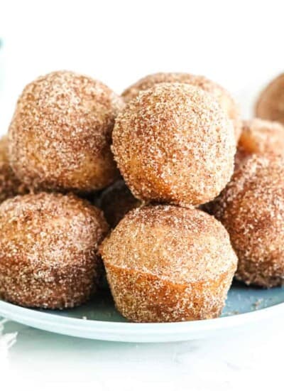 A stack of doughnut holes covered in cinnamon sugar on a plate from the side