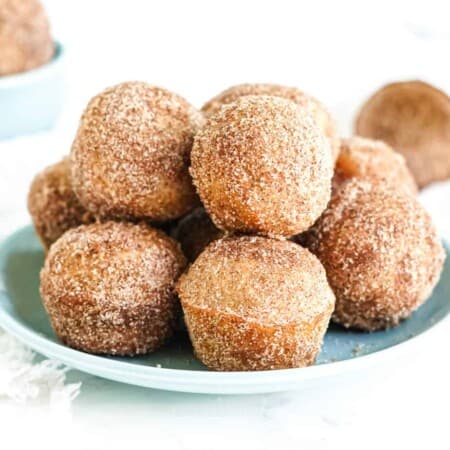 A stack of doughnut holes covered in cinnamon sugar on a plate from the side