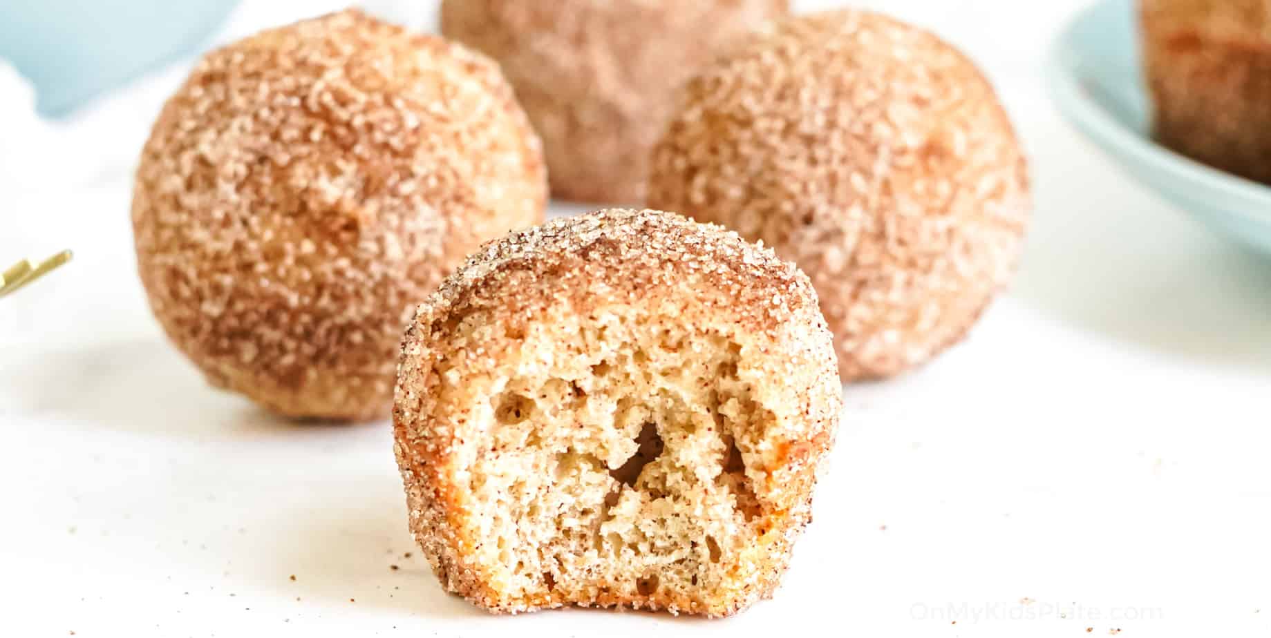 Close up from the side of several apple cider doughnut holes, the front doughnut missing a bite.