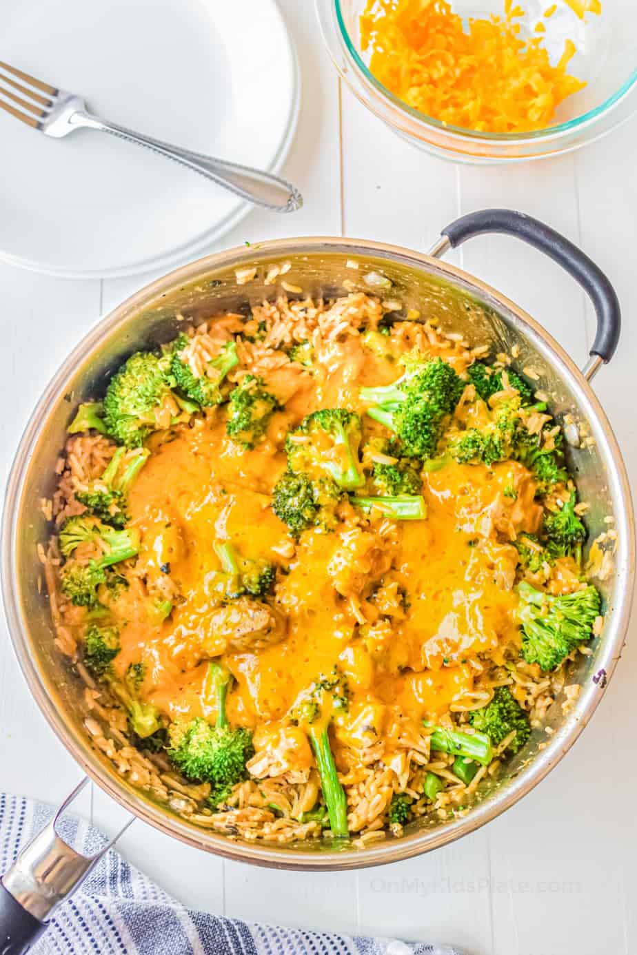 Melted cheese over broccoli, chicken and rice in a pan.