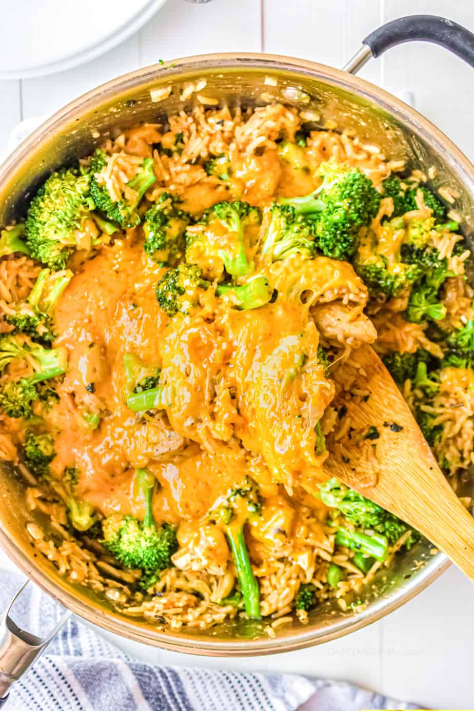 Chicken, cheese, broccoli and rice in a pan with a wooden spoon from overhead.
