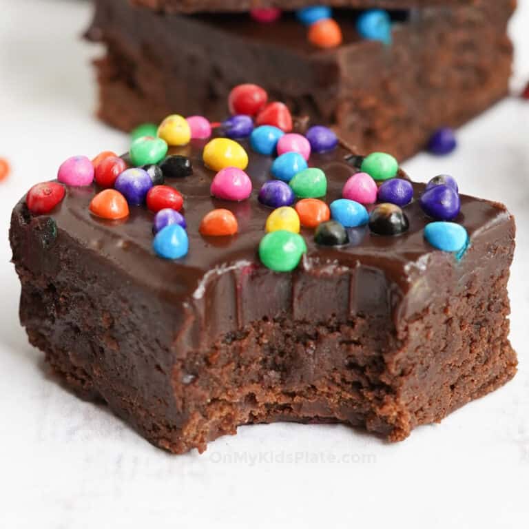 Close up a a thick frosted brownie with rainbow sprinkles and a bite taken out of it.