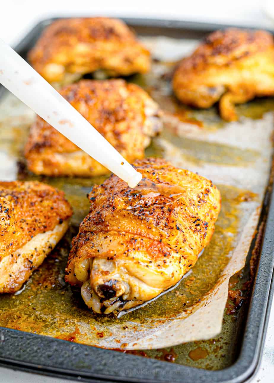 Juicy crispy brown chicken thighs being basted on the pan with the chicken juices.