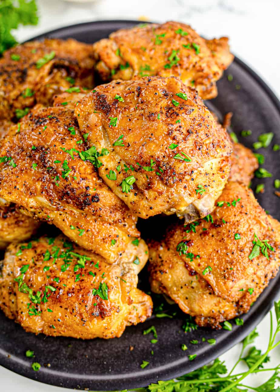 Golden brown juicy chicken thighs piled on a round plate