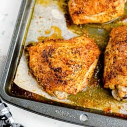 Golden brown baked chicken thighs sitting in juices on the pan close up