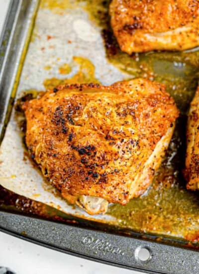 Golden brown baked chicken thighs sitting in juices on the pan close up