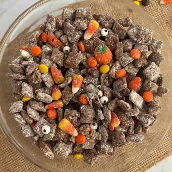 A large bowl from overhead fully of chocolate peanut butter covered cereal also known as muddy buddies, candy corn and candy pumpkins